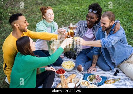 Glückliche junge Freunde toasten Trinkgläser und Flasche im Park Stockfoto