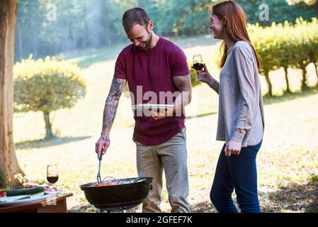 Lächelndes junges Paar, das sich unterhielt, während es in der Nähe des Grills im Park stand Stockfoto