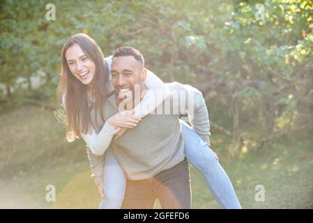 Lächelnder junger Mann, der seinem Partner eine Huckepack-Fahrt gibt Stockfoto