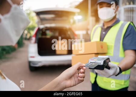 Asiatische Lieferung Mann mit Kreditkarte Swiping Maschine zu bezahlen. Hand mit Kreditkarte wischen durch Terminal für die Zahlung auf der Außenseite des Lagers. Stockfoto