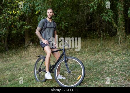 Nachdenklicher junger Mann, der im Wald auf dem Fahrrad sitzt Stockfoto