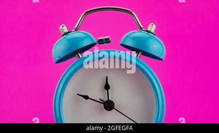 Blauer Wecker auf rosa Hintergrund vor zwölf Uhr am Silvesterabend des Gesichts des schönen Weckers zeigt Mitternacht liebenswert Neujahr cele Stockfoto