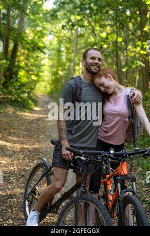 Lächelndes junges Paar, das mit Fahrrädern im Wald steht Stockfoto
