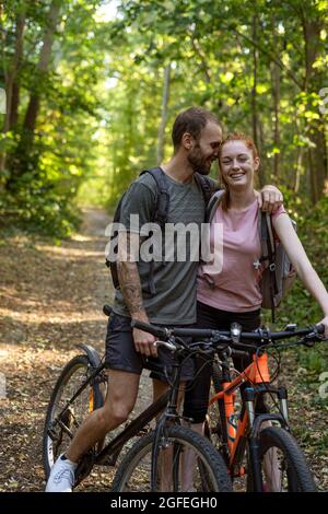 Lächelndes junges Paar, das mit Fahrrädern im Wald steht Stockfoto