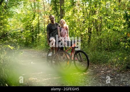 Lächelndes junges Paar, das mit Fahrrädern im Wald steht Stockfoto