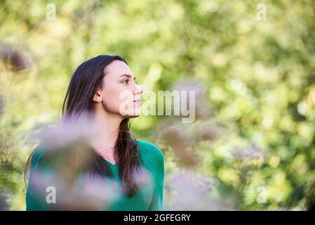 Nachdenkliche junge Frau, die im öffentlichen Park steht Stockfoto