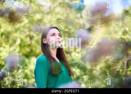 Nachdenkliche junge Frau, die im öffentlichen Park steht Stockfoto