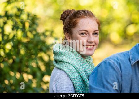 Porträt einer lächelnden jungen Frau, die im öffentlichen Park sitzt Stockfoto