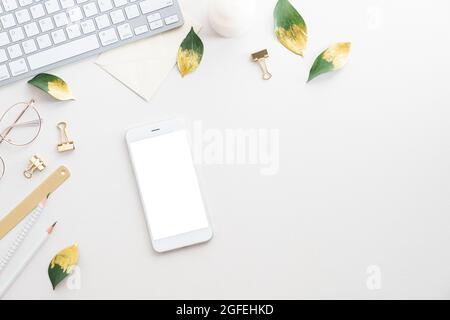 Eleganter, femininer Arbeitsplatz. Smartphone mit leerem Bildschirm, Büromaterial, Computertastatur auf weißem Hintergrund. Flach liegend, Draufsicht, Kopierraster Stockfoto