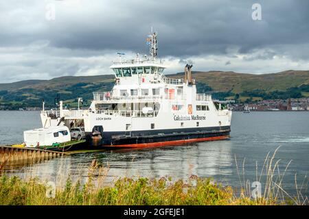 Ein Auto, das einen Wohnwagen auf die MV Loch Shira, alias Loch Siora, die Cal-Mac Ro-Ro-Fähre, bei Cumbrae Slip am Firth of Clyde fährt. Largs ist Hintergrund. Stockfoto