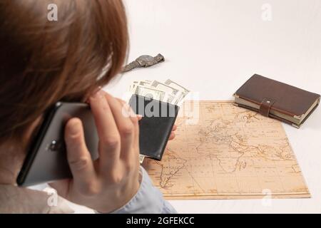 Ein Teil eines Mädchens, das am Telefon spricht, hält sich fest Sie hat eine schwarze Brieftasche mit Geld auf dem Hintergrund Von einem weißen Holztisch mit einem Tagebuch und einem Armbanduhr Stockfoto