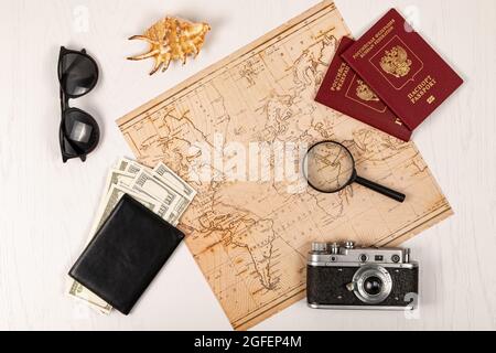 Weltkarte, zwei Pässe, eine Lupe, Geld in einer schwarzen Ledertasche, eine alte Filmkamera, Sonnenbrille und eine Schale auf einem weißen Holztisch. sel Stockfoto
