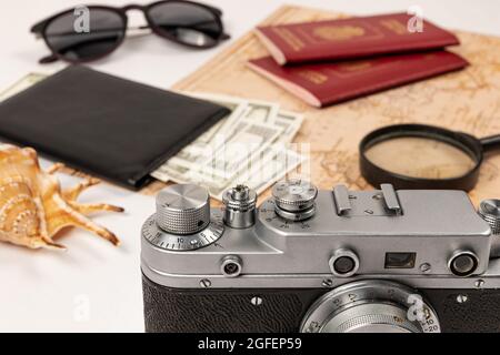 Weltkarte, zwei Pässe, eine Lupe, Geld in einer schwarzen Ledertasche, eine alte Filmkamera, Sonnenbrille und eine Schale auf einem weißen Holztisch. sel Stockfoto