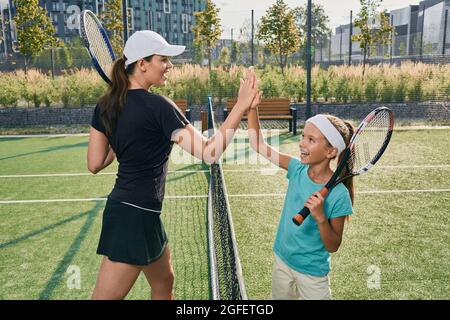 Das Kind gibt ihrem Trainer fünf, nachdem er Tennis gespielt hat. Tennistraining für Kinder auf dem Freiluftplatz Stockfoto