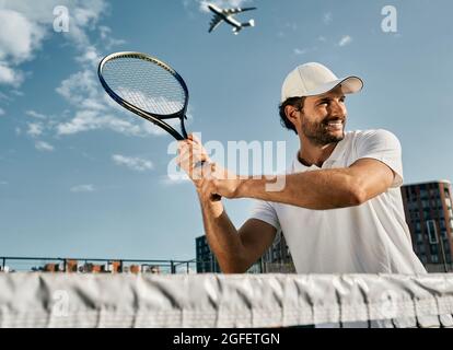 Schöner Tennisspieler während des Matchspiels mit Tennisschläger in den Händen, bevor er über den Hintergrund des blauen Himmels schoss. Tennisspiel spielen Stockfoto