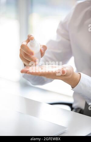 Junger Geschäftsmann, der im Büro Handdesinfektionsmittel verwendet Stockfoto