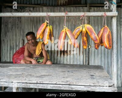 Ambon Island, Indonesien - 11. Februar 2018: Ein Mann verkauft eine riesige Orangenbanane. Bananen hängen an einem Marktstand in einer kleinen Stadt auf der Insel Ambon, Stockfoto