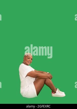 Vertikales Porträt einer lächelnden, schönen Afro-Amerikanerin, die Sportswear-Sitze auf einem grünen Hintergrund trägt Stockfoto