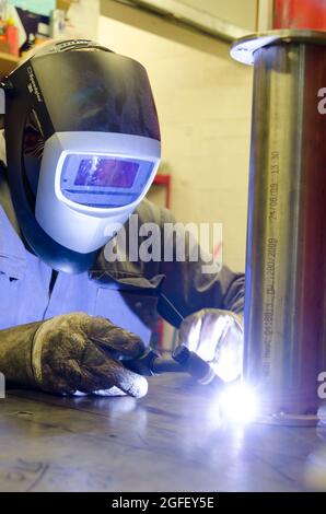 Man WIG-Schweißen Eines Edelstahlflansches an Ein Edelstahlrohr. Vollständige PSA-Gesichtsmaske und Handschuhe werden getragen. Stockfoto