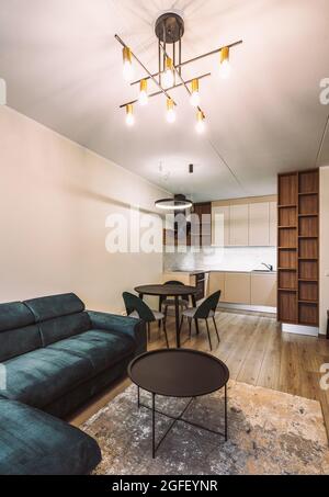 Moderne helle Innenausstattung des renovierten Luxus-Studio-Apartments. Stilvolle beigefarbene Küche. Wohnzimmer mit neuen Möbeln. Gemütliche Couch. Tisch und Stühle. Stockfoto
