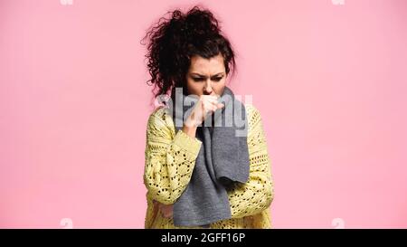 Erkrankte Frau in Strickpullover und Schal hustet isoliert auf rosa Stockfoto