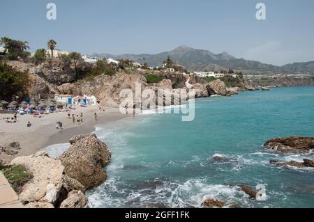 Kleine Bucht im Mittelmeer, Nerja, Costa del Sol, Provinz Malaga, Andalusien, Spanien. Blick auf die Berge, Badegäste, Sonnenschirme, Liegen Stockfoto