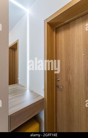 Modernes Interieur der modernen Wohnung. Beigefarbene Wände. Eingangstür aus Holz. Spiegel mit Licht. Stockfoto