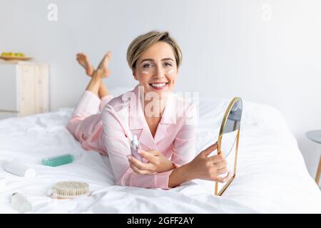 Porträt einer lächelnden Frau mit Spiegel und cremefarbener Flasche Stockfoto