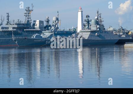 KRONSTADT, RUSSLAND - 11. AUGUST 2021: Antiker Leuchtturm unter den Kriegsschiffen der baltischen Flotte an einem sonnigen Morgen Stockfoto