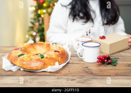 Roscón de Reyes (typisch spanisch süß) ganz auf Holztisch mit Weihnachtsbaum im Hintergrund. Weihnachtsbonbons. Stockfoto