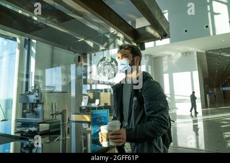 Arnavutkoy, Istanbul, Türkei - 03.08.2021: Ein gutaussehender Mann mit Schutzmaske, der vor der Abflugzeit Starbucks-Kaffee am Flughafen Istanbul kauft Stockfoto