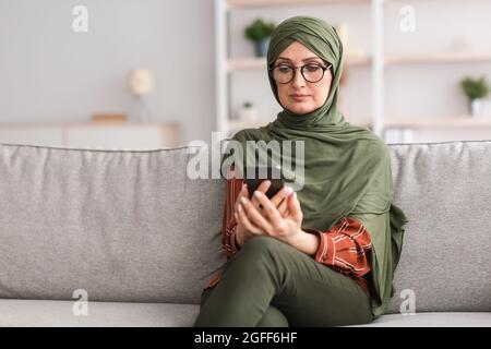 Reife Islamische Frau Mit Smartphone Tragen Brillen Zu Hause Stockfoto