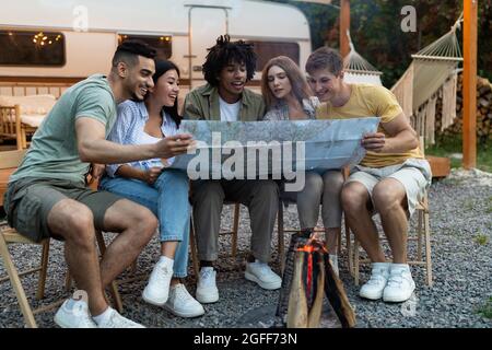 Diverse junge Menschen sitzen am Lagerfeuer, überprüfen die Karte, finden ihr nächstes Reiseziel, machen Herbstferien Stockfoto