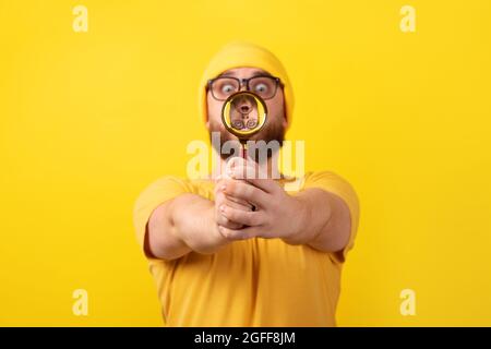 Schockierter Mann, der durch Lupenglas auf gelbem Hintergrund schaute Stockfoto