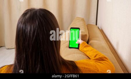 Frau mit langen, lockeren Haaren hält ein Smartphone mit grünem Bildschirm Stockfoto