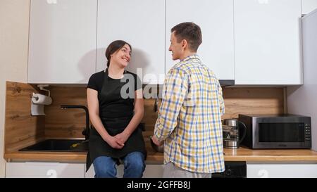 Die Frau sitzt auf dem Tisch, der Mann steht neben ihm und rührt Teig Stockfoto