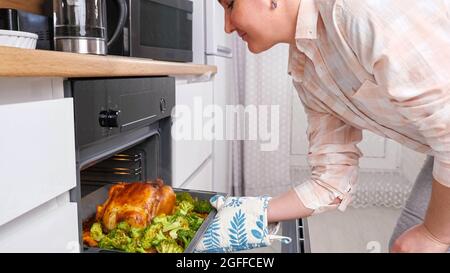Die Frau nimmt knuspriges Huhn auf einem Backblech aus dem Ofen Stockfoto