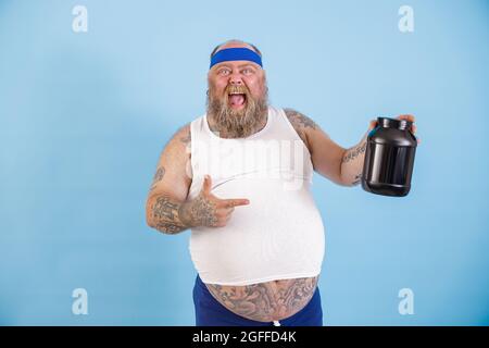 Fröhlich übergewichtigen Mann präsentiert große Flasche Nährstoffergänzung auf hellblauem Hintergrund Stockfoto