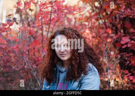 Nahaufnahme Frau Porträt Konzept. Braunhaarige kurvige Frau im Herbstwald mit rotem Busch auf dem Hintergrund Stockfoto