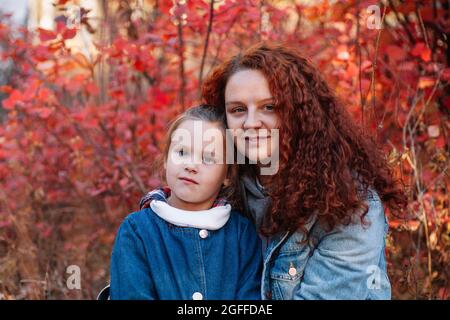 Close up glücklich Familie Konzept. Lächelnde Frau mit kurvigen Haaren und hübsches Mädchen auf Herbst Wald Hintergrund. Glückliche Mutterschaft Stockfoto