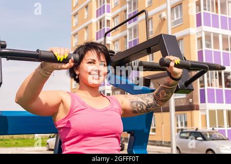 Junge Frau, die im Stadthof Übungen mit einem Brustpresse-Gym-Gerät durchführt Stockfoto