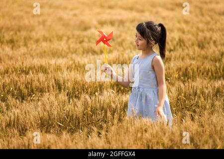 Kleines Mädchen spielt mit Papierwindmühle im Weizenfeld Stockfoto