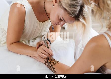 Künstlerin, die Henna-Tätowierung auf Frauenhänden anwendet. Mehndi ist traditionelle indische dekorative Kunst, Hand mit floralen Mehendi. Beauty-Zeichnung für Hochzeiten und Stockfoto