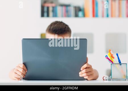 Kleiner Junge sitzt am Tisch mit Laptop und bereitet sich auf die Schule vor. Online-Bildungskonzept Stockfoto