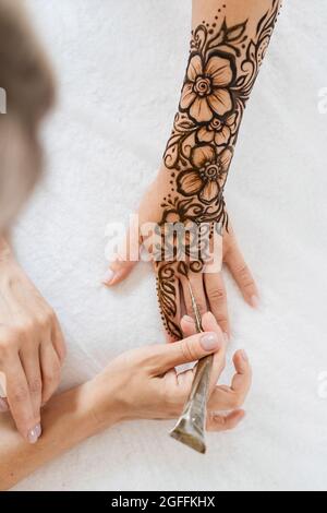 Künstlerin, die Henna-Tätowierung auf Frauenhänden anwendet. Mehndi ist traditionelle indische dekorative Kunst, Hand mit floralen Mehendi. Beauty-Zeichnung für Hochzeiten und Stockfoto