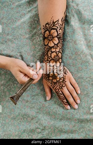 Künstlerin, die Henna-Tätowierung auf Frauenhänden anwendet. Mehndi ist traditionelle indische dekorative Kunst, Hand mit floralen Mehendi. Beauty-Zeichnung für Hochzeiten und Stockfoto