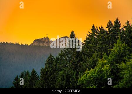 Blick auf das Wanderziel am Kampenwandkreuz bei einem wunderbaren goldenen Stundenlicht von weitem auf den Gipfel des Alpengipfes. Stockfoto