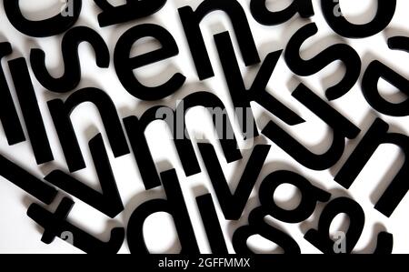 Zufällig angeordnete schwarze Holzbuchstaben auf weißem Hintergrund. Stockfoto