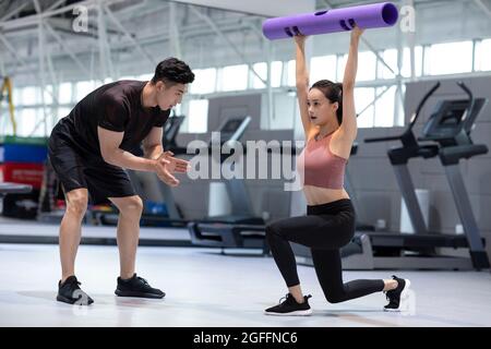Junge Frau, die im Fitnessstudio mit Personal Trainer trainiert Stockfoto