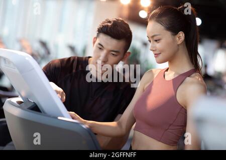 Junge Frau, die im Fitnessstudio mit Personal Trainer trainiert Stockfoto